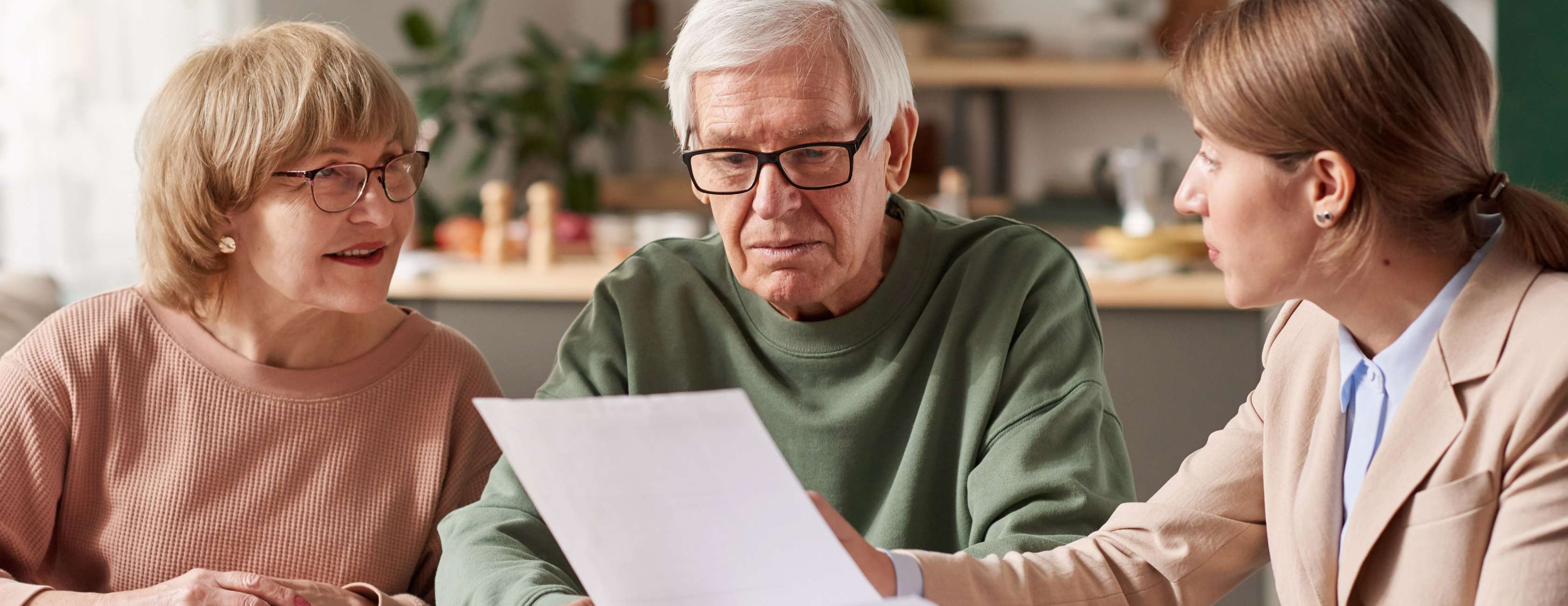 Ein Rentnerehepaar sitz mit einer Beraterin am Tisch und sieht Papiere an