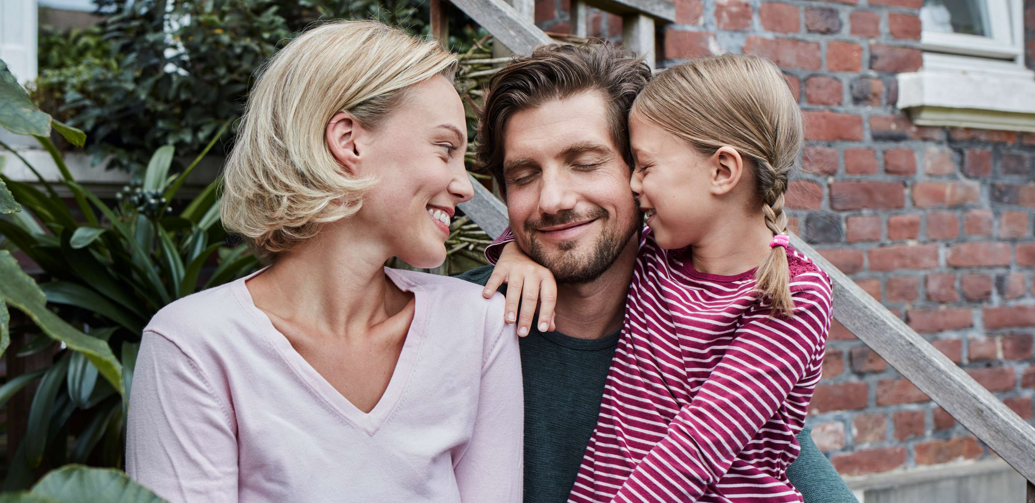 Allianz Risikolebensversicherung: Familie kuschelt vor einem Haus