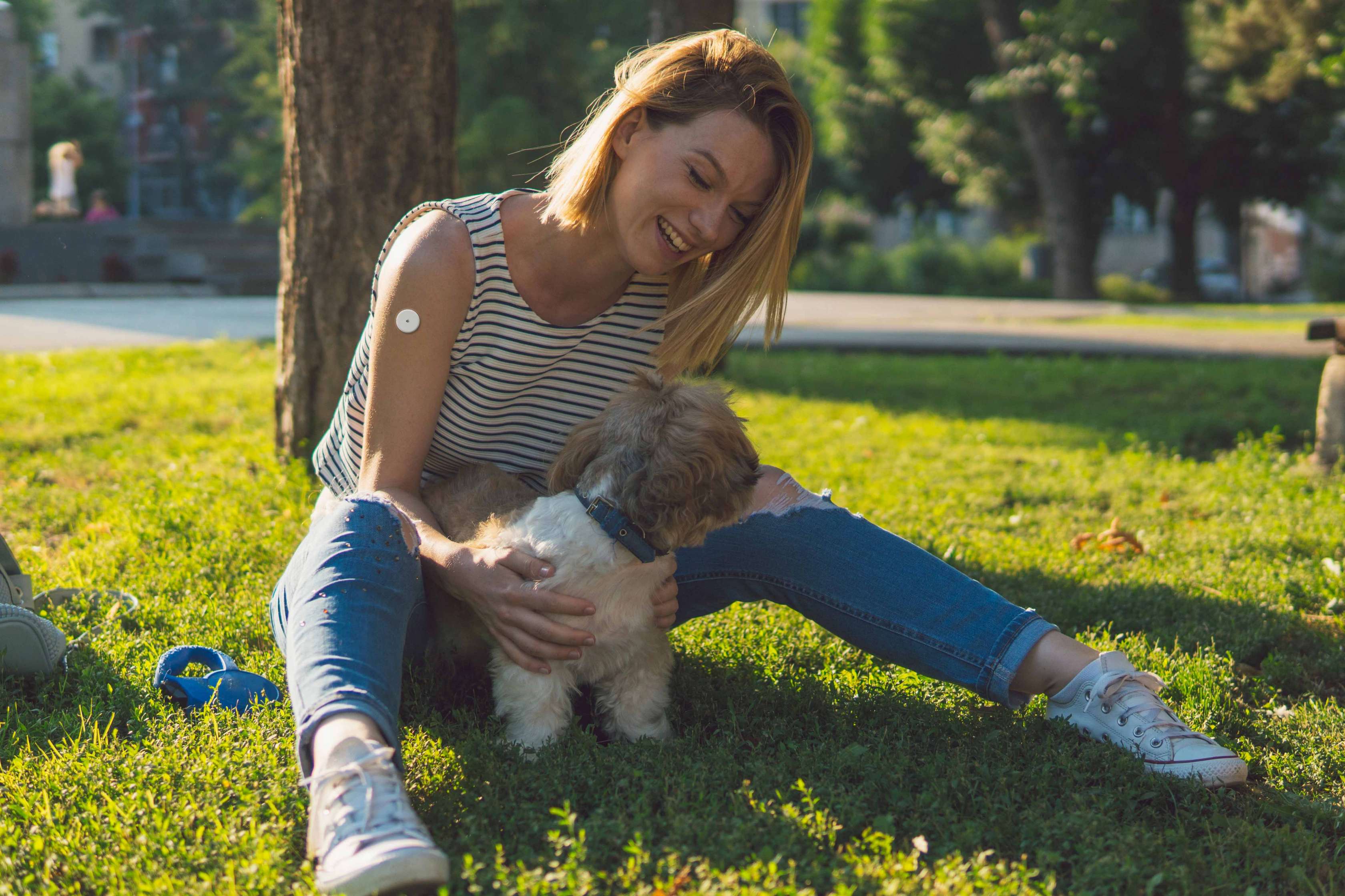 Allianz Risikolebensversicherung für Diabetiker: Eine Frau sitzt lachend mit ihrem Hund auf einer Wiese.