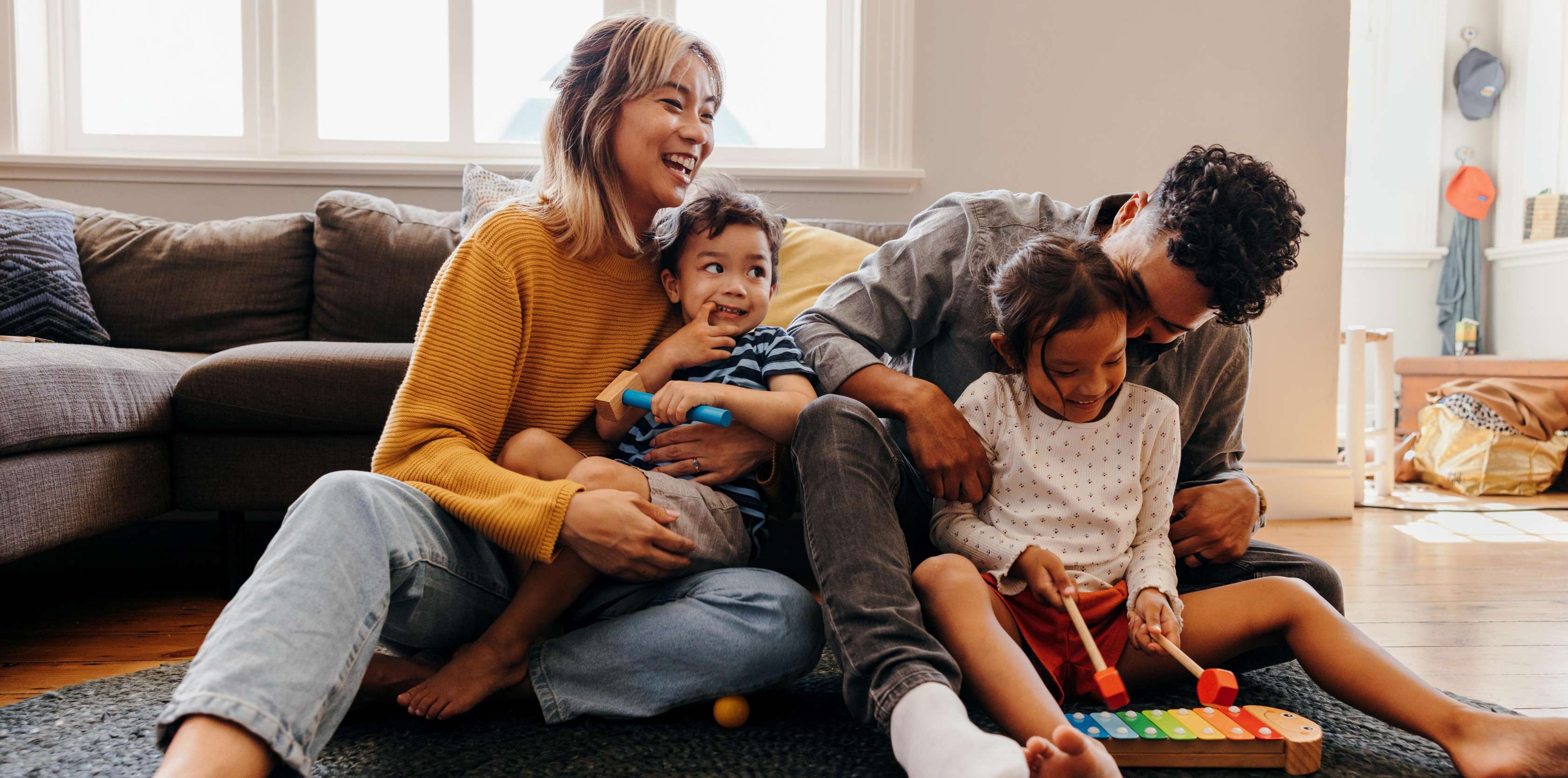 Risikolebensversicherung Versicherungssumme - eine Familie mit zwei Kindern spielt lachend im Wohnzimmer.