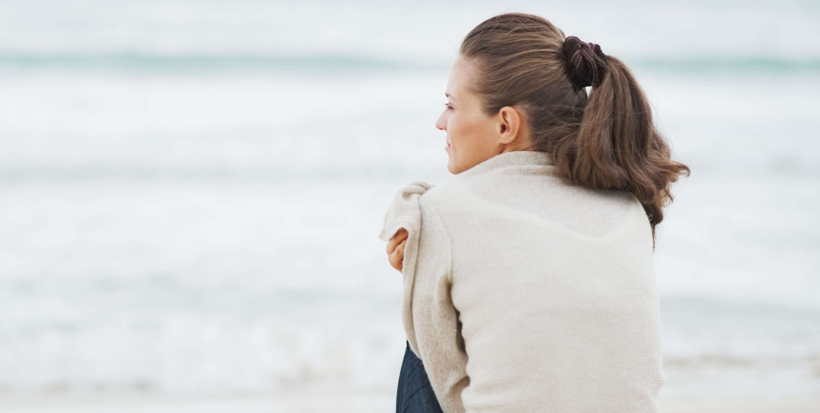 Allianz Seebestattung: Ablauf, Orte und Kosten - Eine Frau sitzt nachdenklich am Meer und blickt in die Ferne.