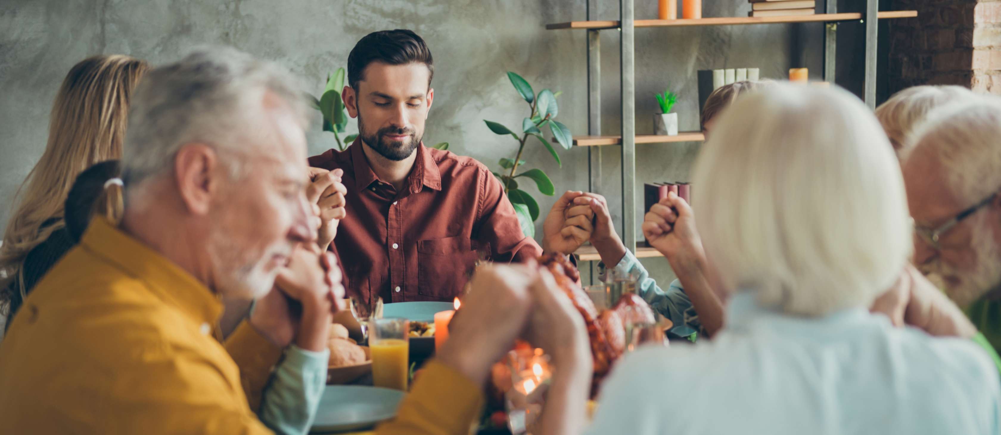Allianz Sterbegeldversicherung - Leichenschmaus planen: Eine Familie sitzt zusammen am Tisch und betet.