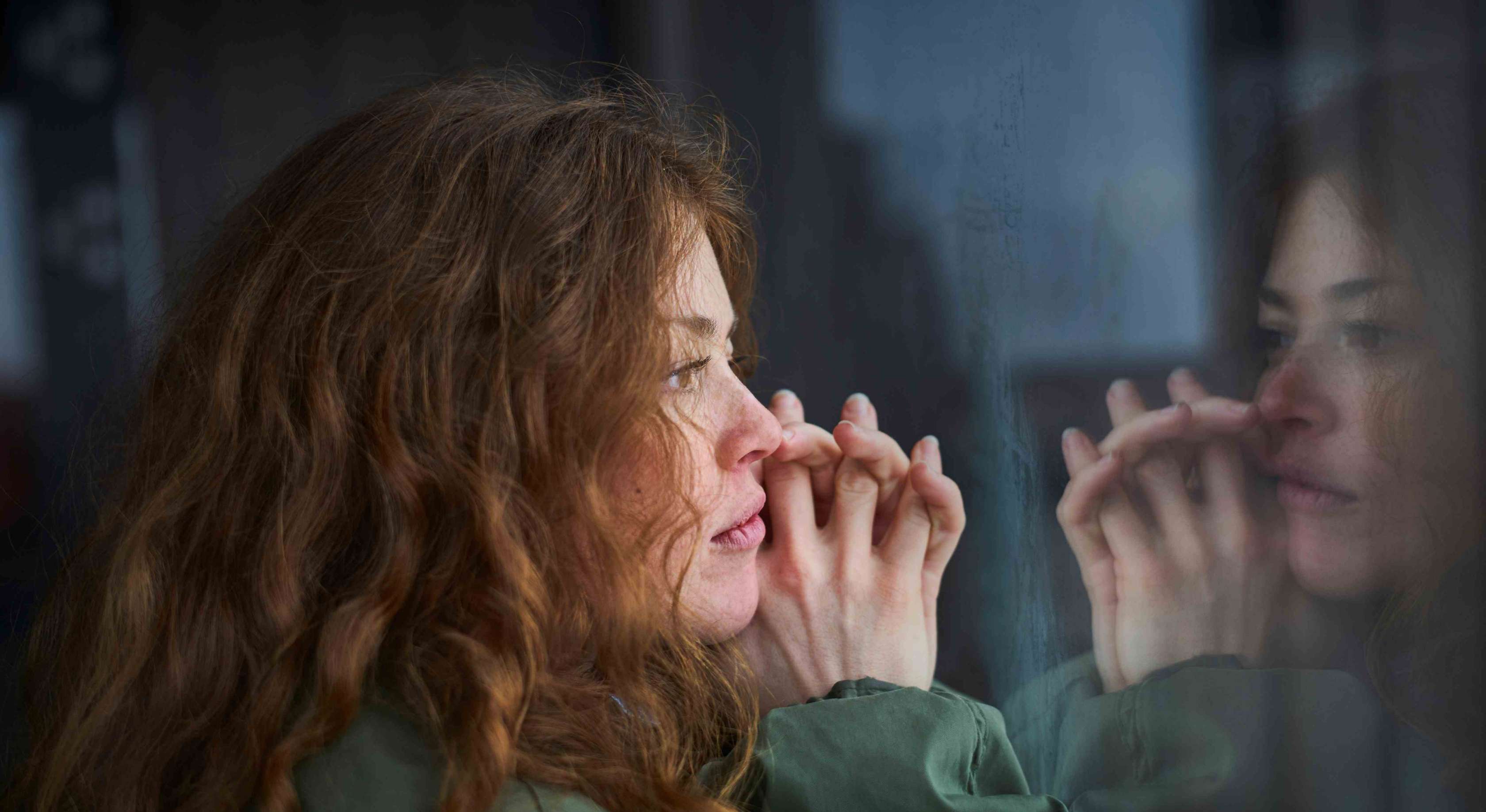 Allianz Sterbegeldversicherung - Sonderurlaub bei Todesfall: Eine Frau sitzt am Fenster und schaut nachdenklich nach draußen.