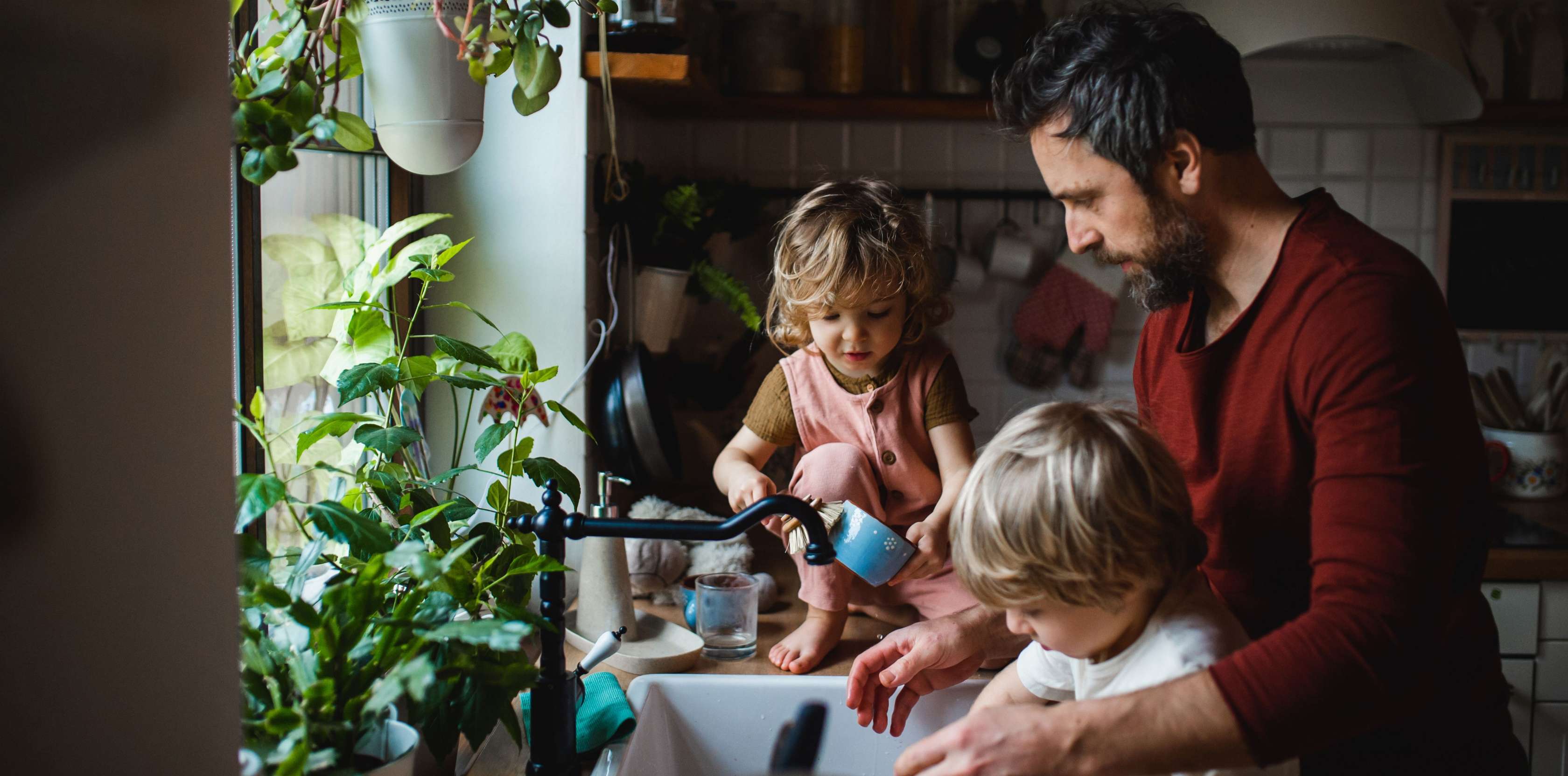 Allianz Todesfallversicherung: Ein Vater steht mit seinen zwei Kindern in der Küche und spült ab.