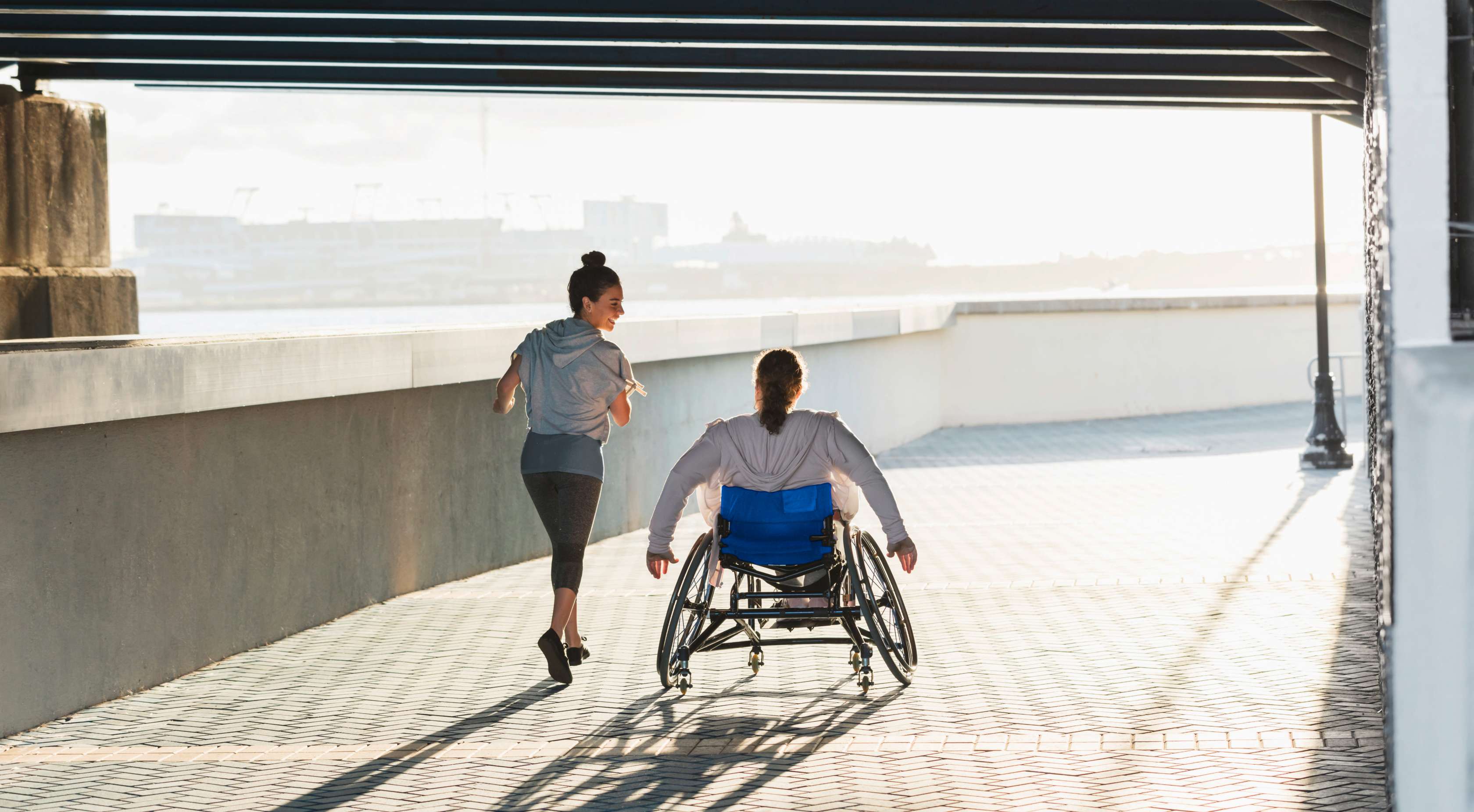 Unfallversicherung: Ein Rollstuhlfahrer fährt neben einer Joggerin auf einem Weg