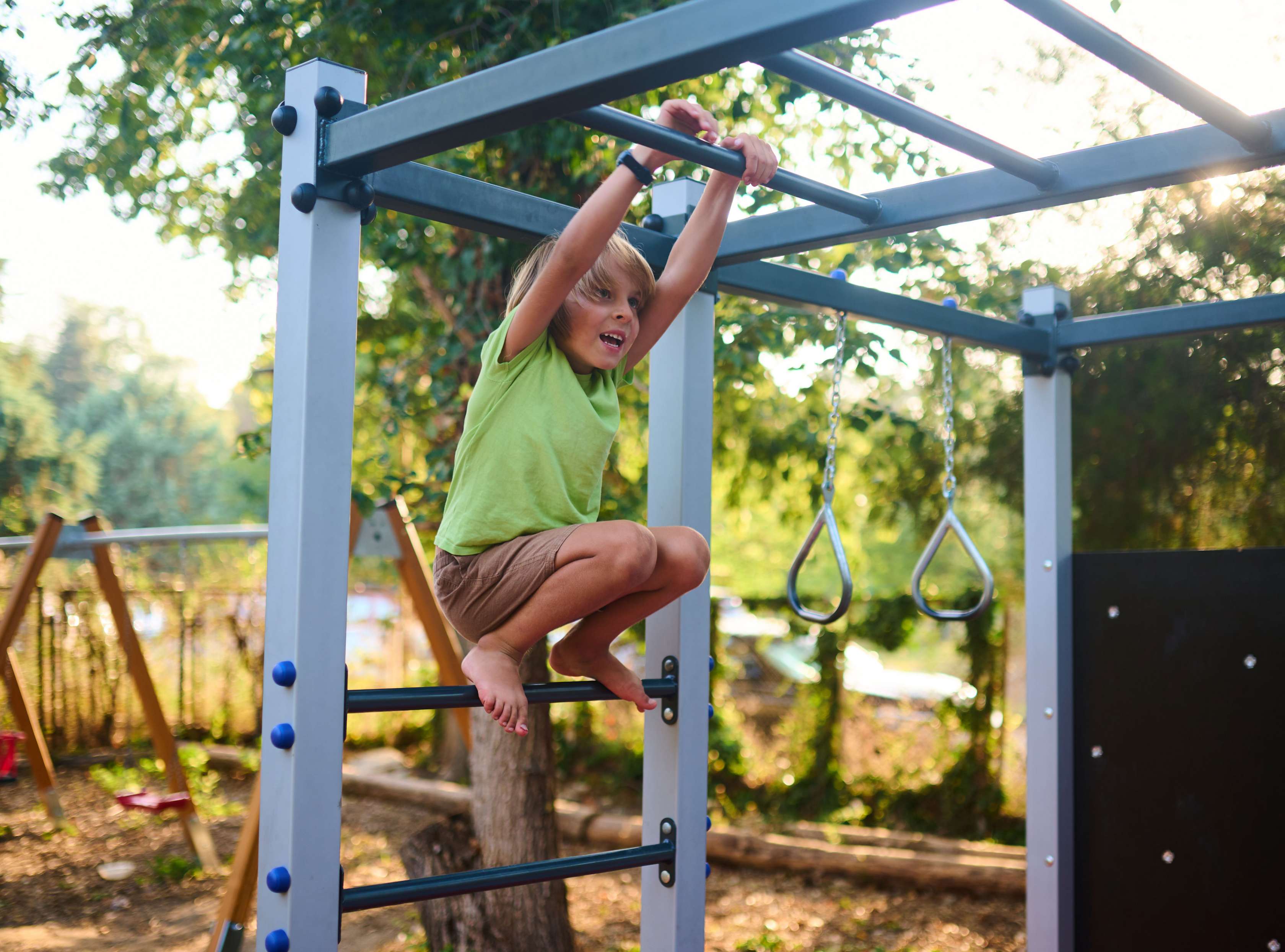 Allianz Private Kinderunfallversicherung: Junge hängt sich an ein Klettergerüst auf einem Spielplatz