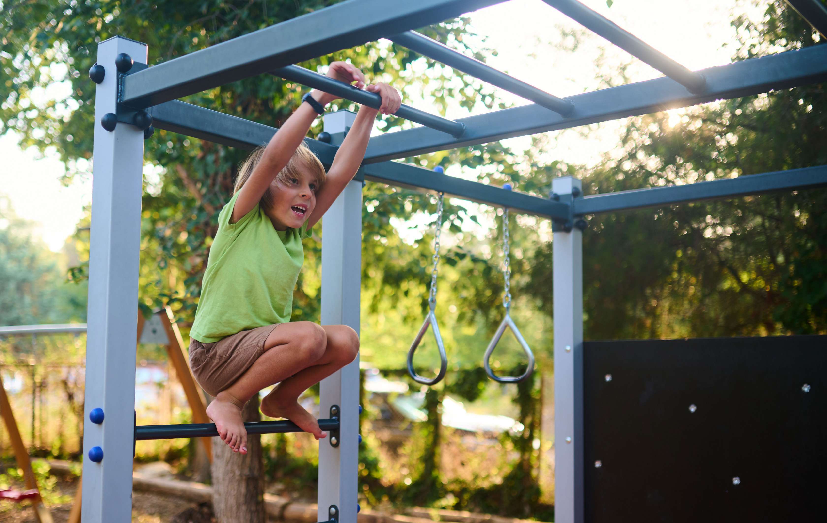 Allianz Private Kinderunfallversicherung: Junge hängt sich an ein Klettergerüst auf einem Spielplatz