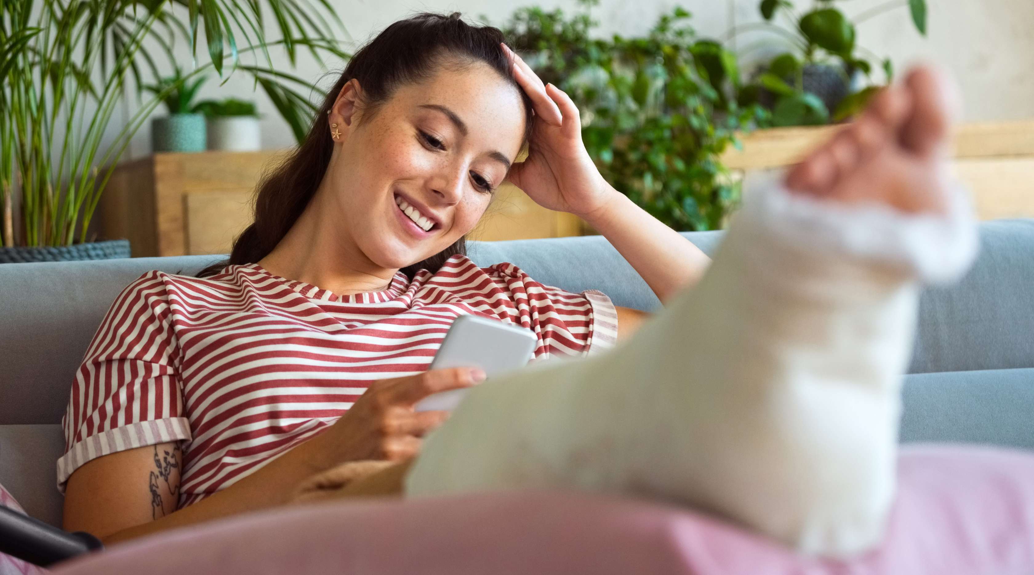 Unfallversicherung für Studierende: Eine Studentin mit einem Gipsbein sitzt zuhause auf dem Sofa