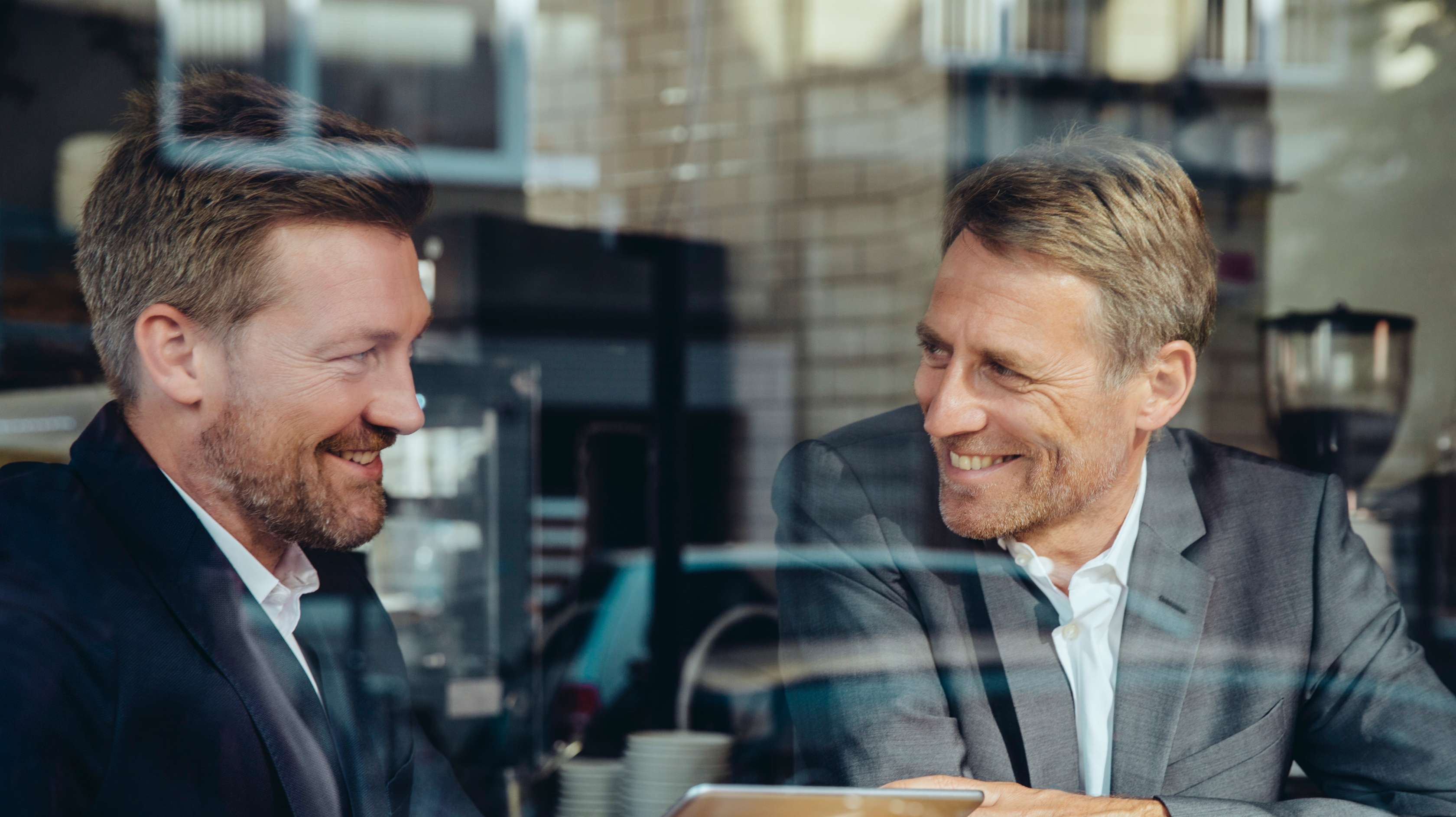 Allianz Vermögenswirksame Leistungen: Zwei Geschäftsmänner sitzen gemeinsam in einer Cafeteria sitzen und unterhalten sich